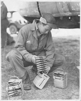 Sgt Dick Arbogast loading machine gun ammunition belt into container.